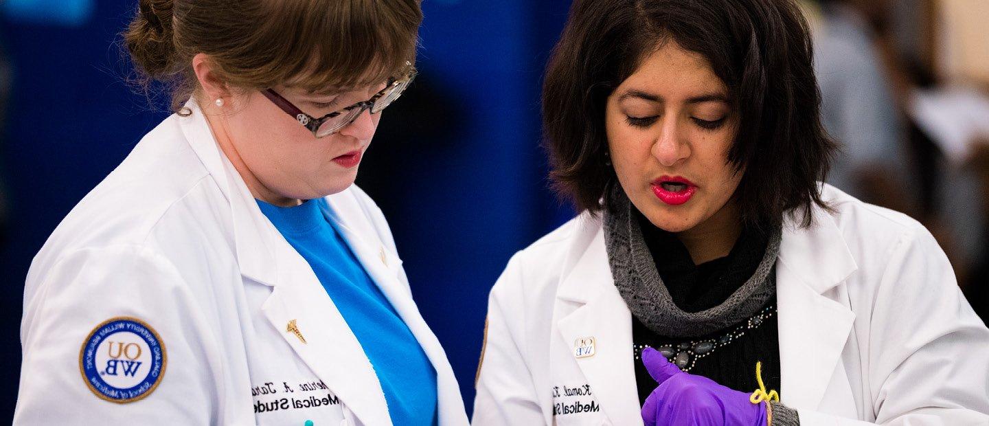 two women wearing white O U W B medical lab coats